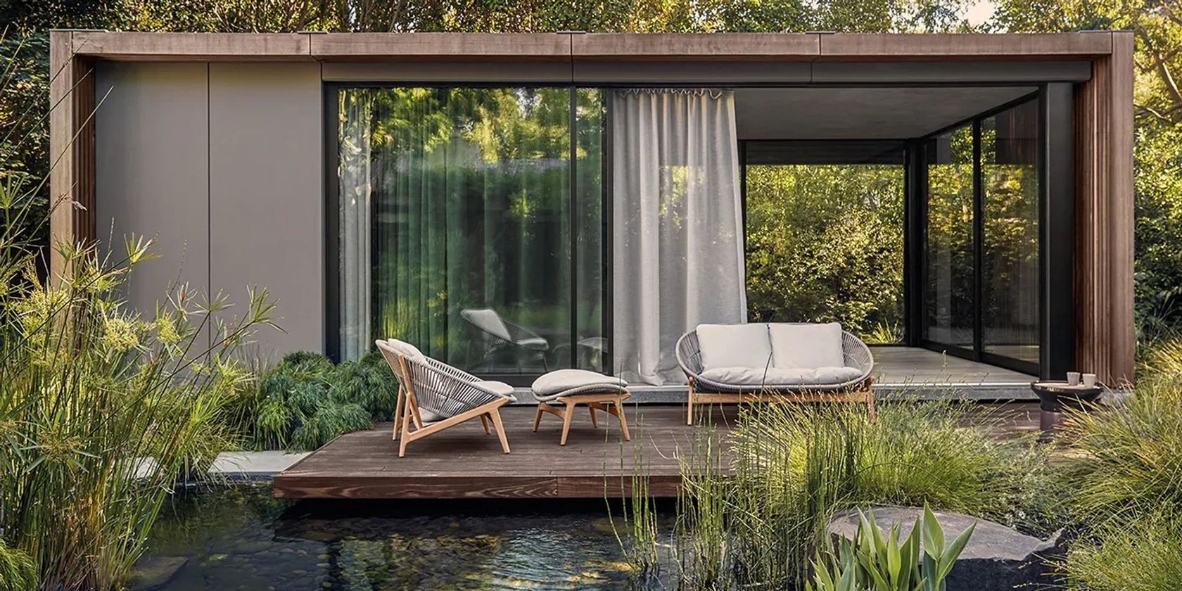 Gloster Bora lounge chairs and sofa on a timber deck beside a garden pond, modern pavilion backdrop
