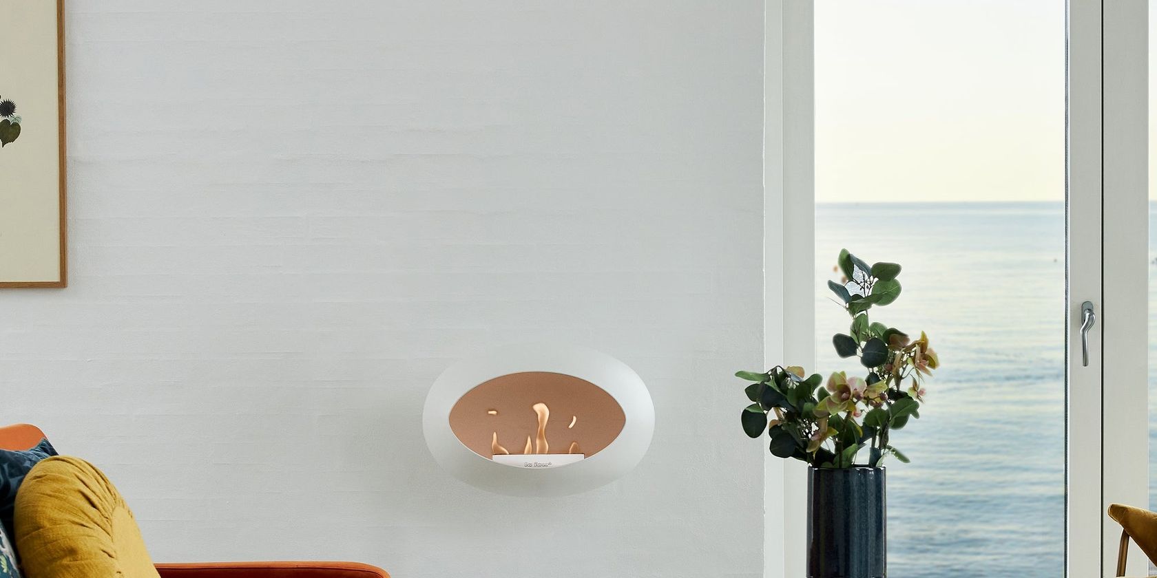 A white Le Feu wall-mounted Dome bio-ethanol fireplace lit in a coastal living room, no people
