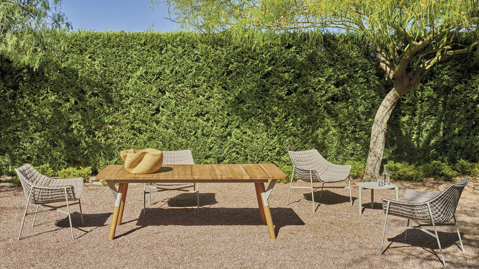 Varaschin Link dining table and woven chairs in a lush garden setting, no people
